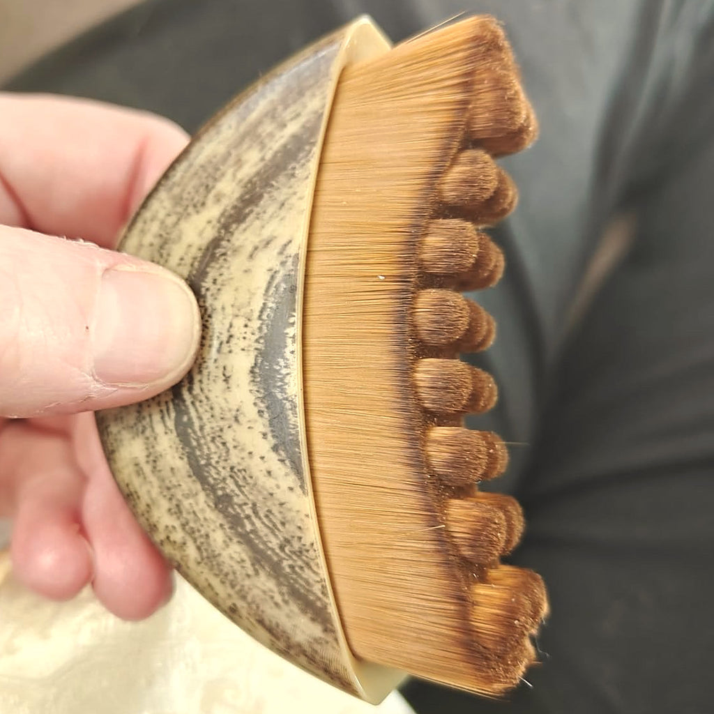 The Cueva Contour Brush resting in an open hand, showing its palm size, speckled cream handle and dense golden bristle fan