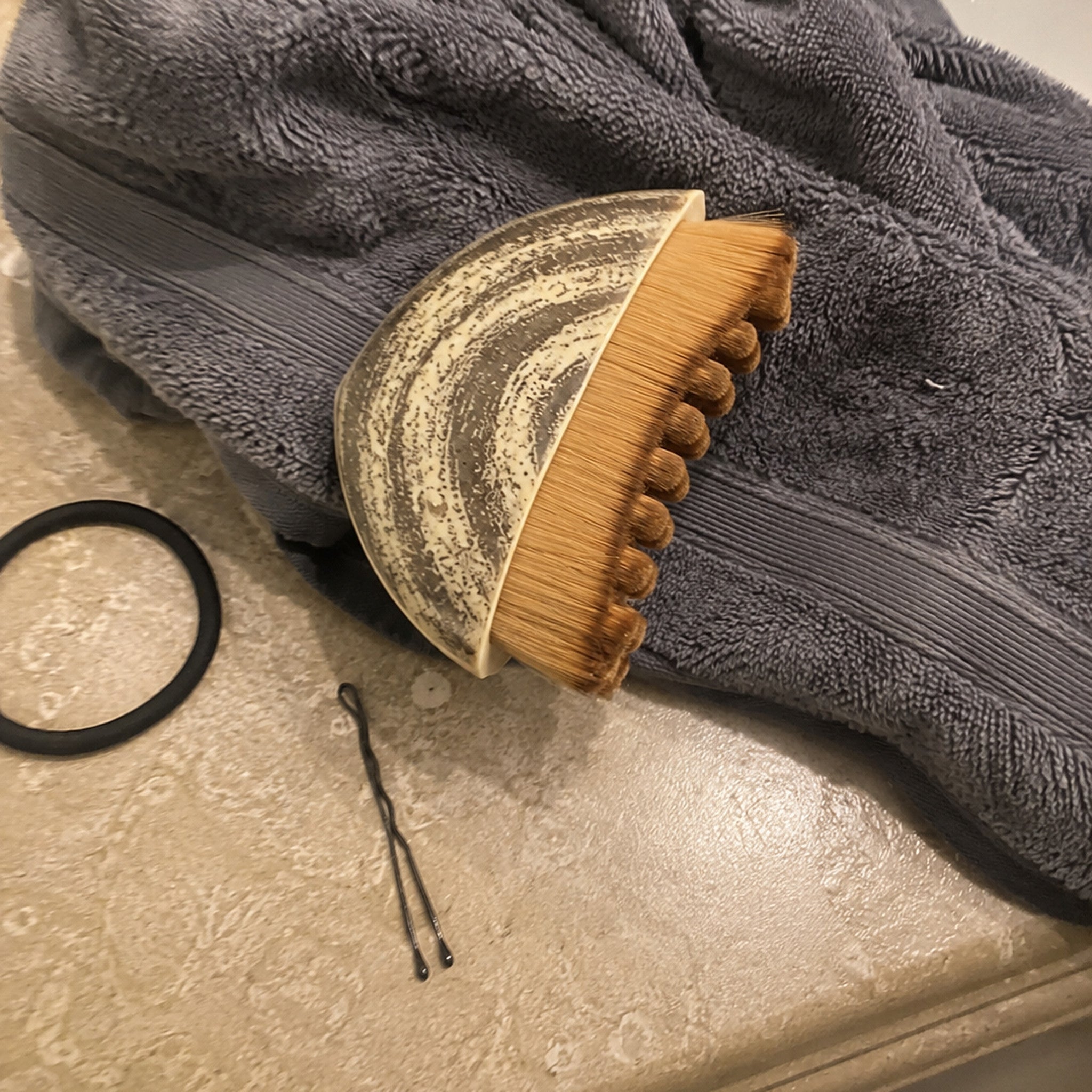 The Cueva Contour Brush on a bathroom counter beside a hair tie and a bobby pin