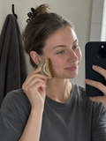 Woman smiling at her reflection in a bathroom mirror while holding the Cueva Contour Brush against her cheekbone